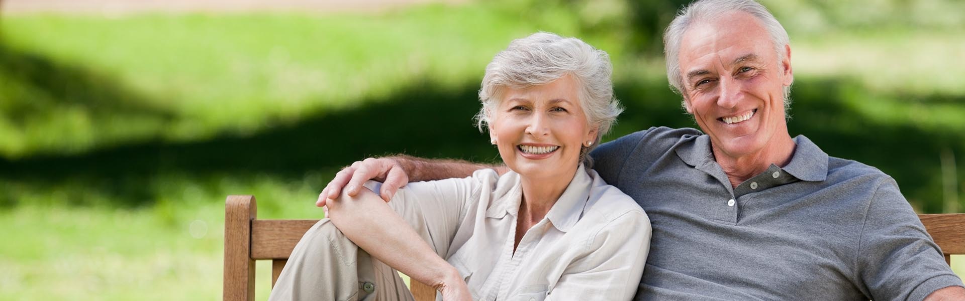 The image depicts an elderly couple sitting together on a bench outdoors during the daytime.